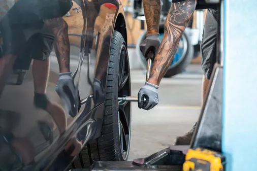 Hände in Arbeitshandschuhen ziehen die Radschrauben an einem Auto mit dem Drehmomentschlüssel an