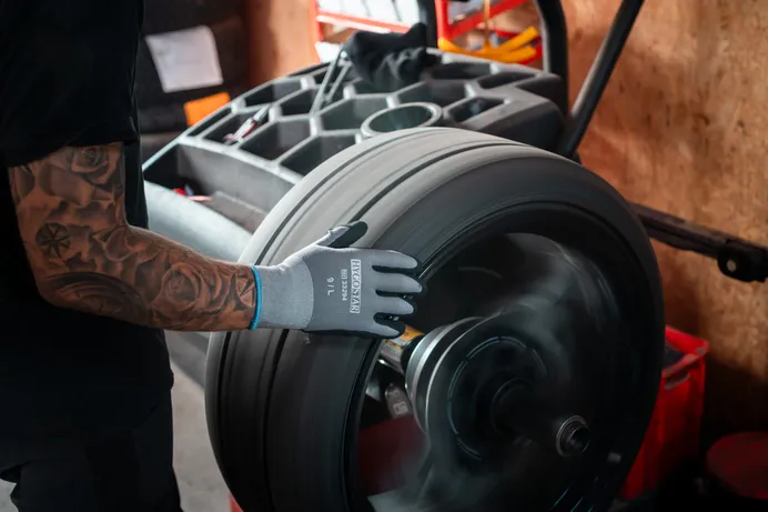 Rad dreht sich auf der Wuchtmaschine, eine Hand mit Arbeitshandschuh liegt auf der Lauffläche